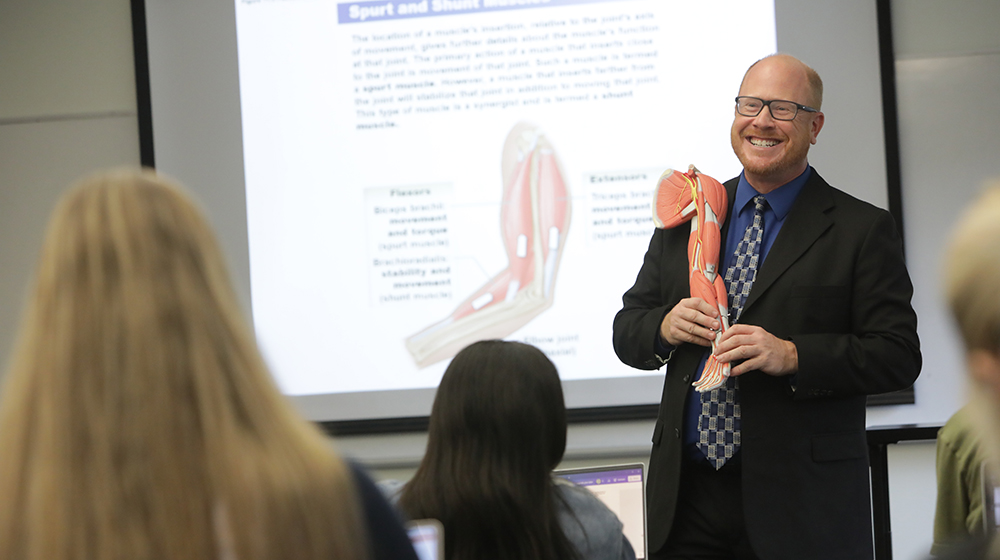 Matt Bruder holds a model arm in front of a classroom